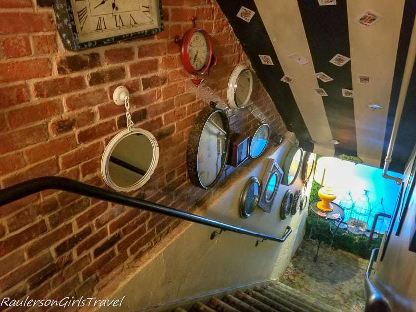 Clocks, mirrors, and cards decorating the wall leading down the stairs at Mad Hatter Bistro