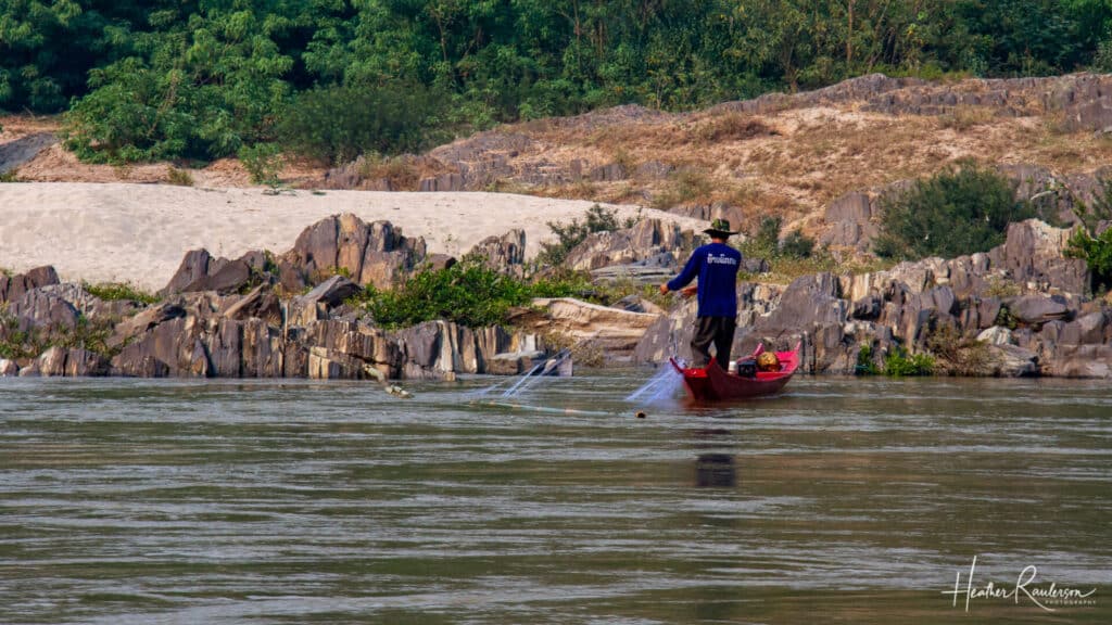 Fisherman casting a net on a red long boat on the Mekong River