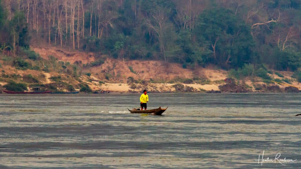 Man on a long boat in the middle of the Mekong River